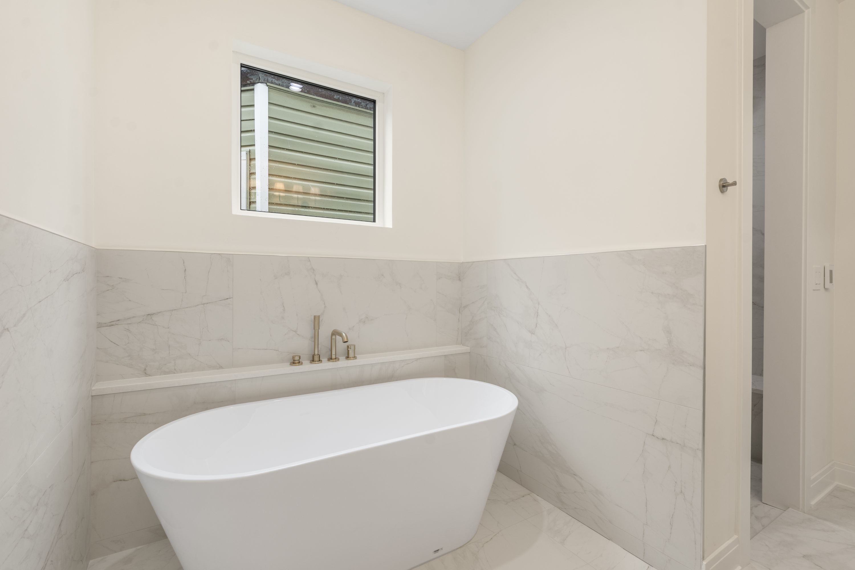 Freestanding primary bathtub with marble tile and brass fixtures